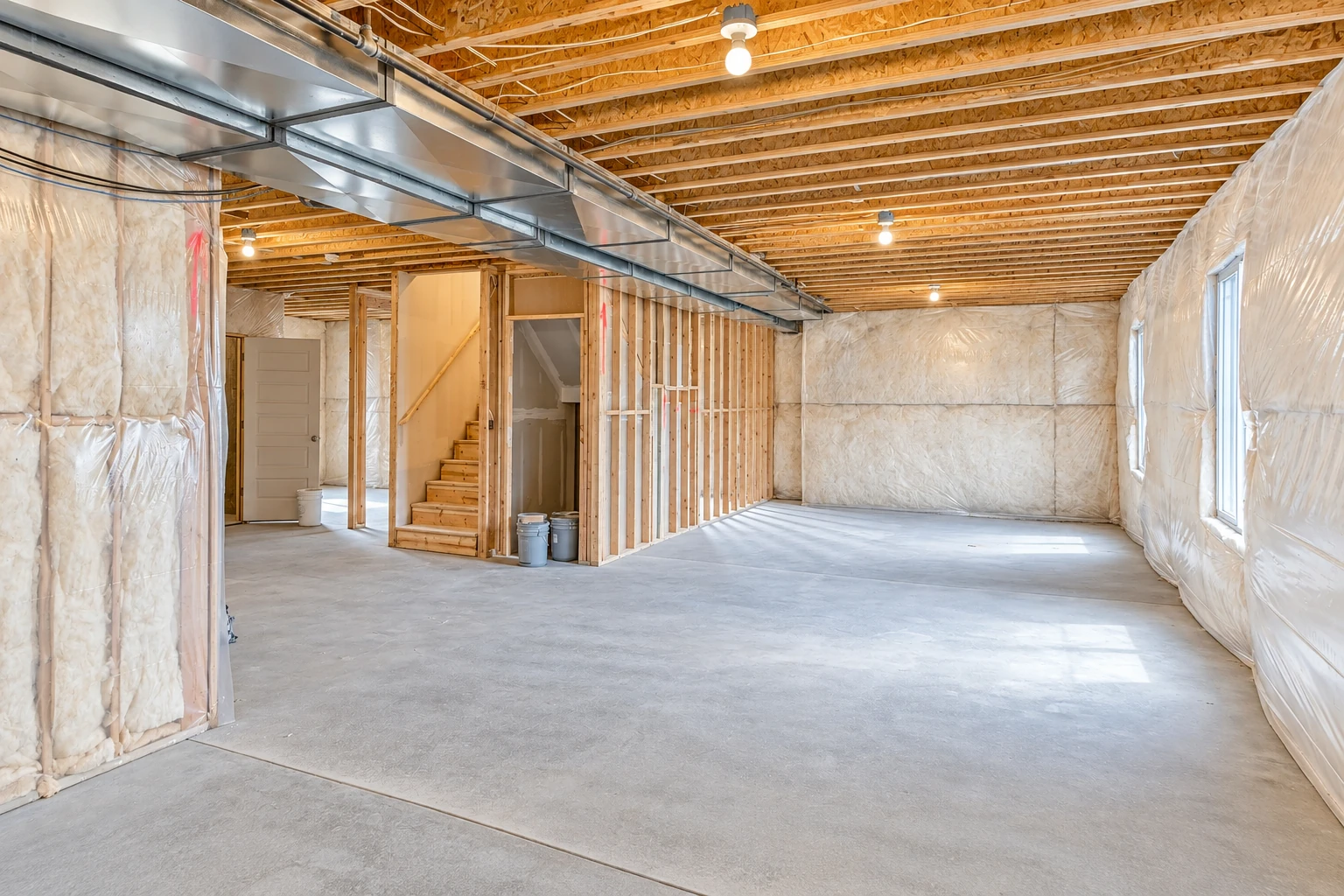 Unfinished basement with insulation lining the walls, exposed ceiling joists, and metal ductwork overhead.